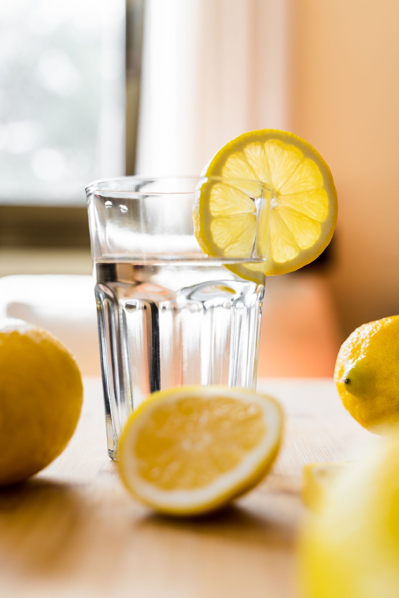 Un grand verre d'eau limpide, une rondelle de citron, sur une table de bois clair.