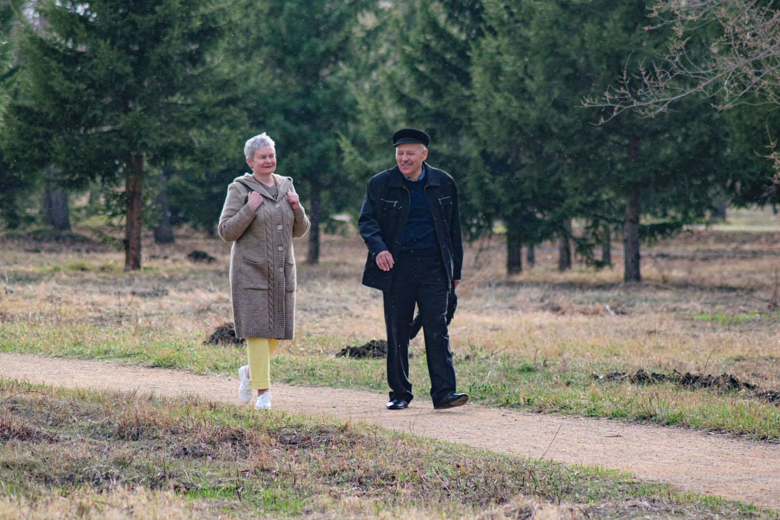 Un couple, la soixantaine, marche d'un bon pas sur un chemin de campagne, au grand air.
